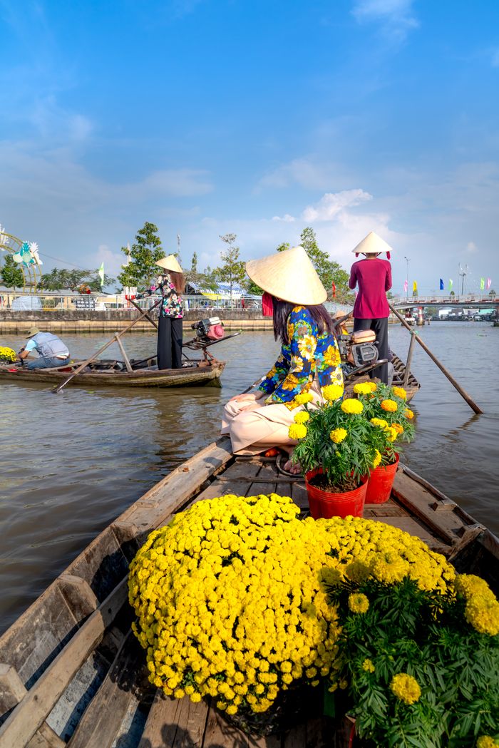 Colorful traditional floating market scene in Vietnam with yellow flowers and conical hats.